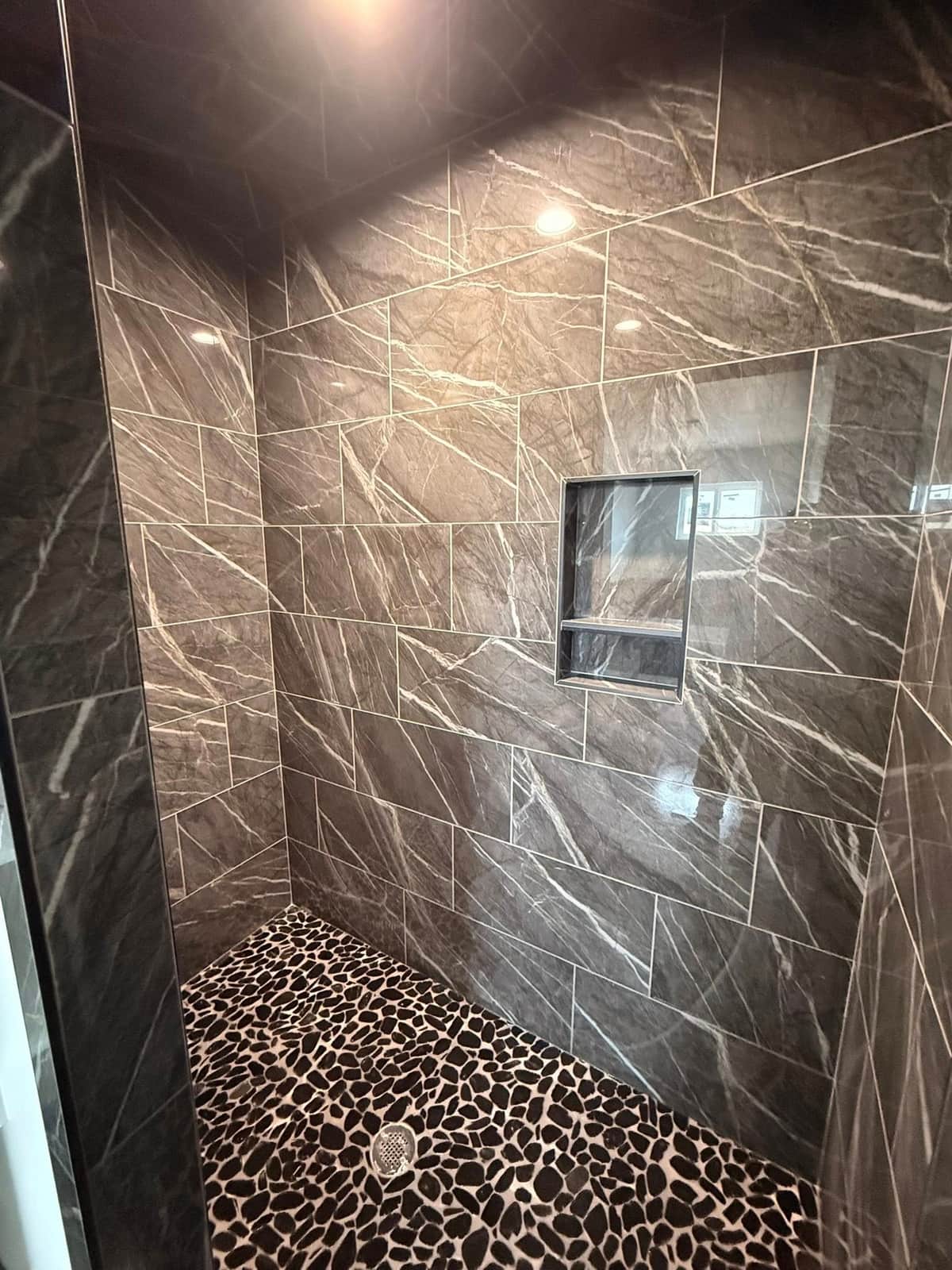 Dark marble shower with pebble stone floor